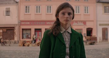 Movie still from “Jojo Rabbit” (2019), directed by Taika Waititi – A woman in a green coat standing in front of a pink building; Medium shot, Over the shoulder angle