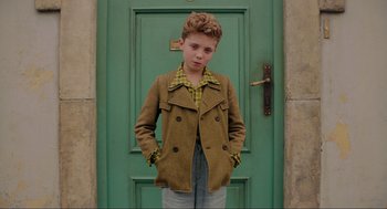 Movie still from “Jojo Rabbit” (2019), directed by Taika Waititi – A young boy standing in front of a green door; Medium shot, High angle