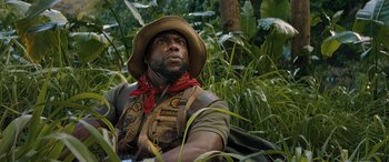 Movie still from “Jumanji: The Next Level” (2019), directed by Jake Kasdan – A man wearing a hat and vest in the woods; Close Up shot, Low angle