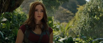 Movie still from “Jumanji: The Next Level” (2019), directed by Jake Kasdan – A beautiful young woman standing next to a lush green forest; Close Up shot, Over the shoulder angle