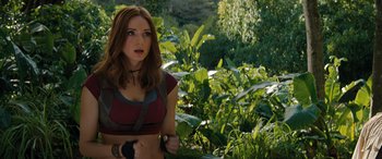 Movie still from “Jumanji: The Next Level” (2019), directed by Jake Kasdan – A beautiful woman standing next to a lush green forest; Medium shot, Over the shoulder angle