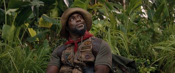 Movie still from “Jumanji: The Next Level” (2019), directed by Jake Kasdan – A man in a hat and vest sitting in the woods; Close Up shot, Low angle