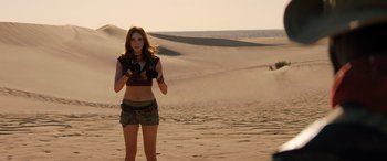 Movie still from “Jumanji: The Next Level” (2019), directed by Jake Kasdan – A woman standing in the sand holding a camera; Wide shot, Over the shoulder angle