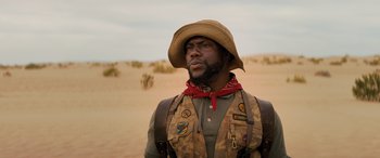 Movie still from “Jumanji: The Next Level” (2019), directed by Jake Kasdan – A man in a hat and vest standing in the desert; Close Up shot, Low angle
