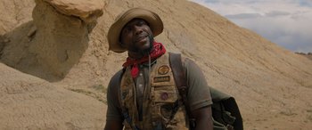 Movie still from “Jumanji: The Next Level” (2019), directed by Jake Kasdan – A man in a cowboy hat standing in front of a cliff; Close Up shot, Low angle