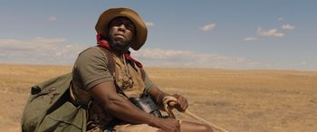 Movie still from “Jumanji: The Next Level” (2019), directed by Jake Kasdan – A man sitting in the middle of a field holding a rope; Close Up shot, Low angle