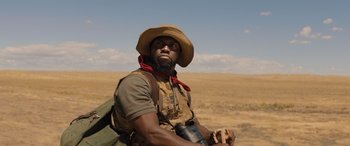 Movie still from “Jumanji: The Next Level” (2019), directed by Jake Kasdan – A man with a hat on holding a camera in a field; Close Up shot, Low angle