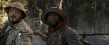 Movie still from “Jumanji: The Next Level” (2019), directed by Jake Kasdan – A man in a hat and vest standing in front of trees; Close Up shot, Low angle