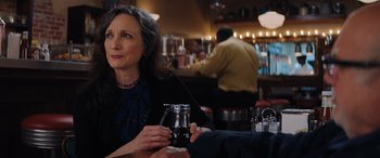 Movie still from “Jumanji: The Next Level” (2019), directed by Jake Kasdan – A woman sitting at a table in front of a glass jar; Medium shot, Over the shoulder angle