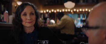 Movie still from “Jumanji: The Next Level” (2019), directed by Jake Kasdan – A woman sitting at a table in front of lights; Close Up shot, Over the shoulder angle