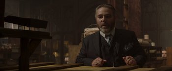 Movie still from “Jungle Cruise” (2021), directed by Jaume Collet-Serra – A man sitting at a table wearing a suit and tie; Medium shot, Over the shoulder angle