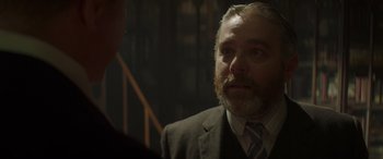 Movie still from “Jungle Cruise” (2021), directed by Jaume Collet-Serra – An older man in a suit and tie looking at the camera; Close Up shot, Over the shoulder angle