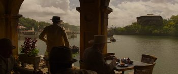 Movie still from “Jungle Cruise” (2021), directed by Jaume Collet-Serra – Two men sitting at a table near a body of water; Wide shot, High angle