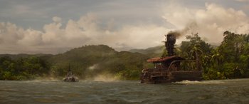Movie still from “Jungle Cruise” (2021), directed by Jaume Collet-Serra – A boat floating on top of a body of water near trees; Extreme Wide shot, Low angle