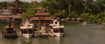 Movie still from “Jungle Cruise” (2021), directed by Jaume Collet-Serra – A group of boats docked at a pier in the middle of a lake; Extreme Wide shot, High angle
