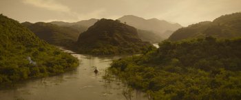 Movie still from “Jungle Cruise” (2021), directed by Jaume Collet-Serra – A person in a boat on a river with mountains in the background; Extreme Wide shot, High angle