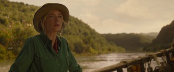 Movie still from “Jungle Cruise” (2021), directed by Jaume Collet-Serra – A woman wearing a hat standing next to a body of water; Medium shot, Over the shoulder angle