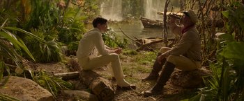 Movie still from “Jungle Cruise” (2021), directed by Jaume Collet-Serra – A man sitting on top of a tree stump; Wide shot, Over the shoulder angle