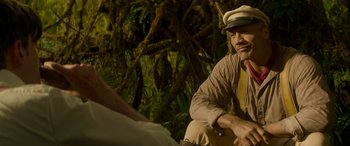 Movie still from “Jungle Cruise” (2021), directed by Jaume Collet-Serra – A man sitting on the ground in front of a tree; Medium shot, Over the shoulder angle