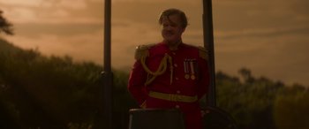 Movie still from “Jungle Cruise” (2021), directed by Jaume Collet-Serra – A man in a red military uniform standing next to a pole; Medium shot, Low angle