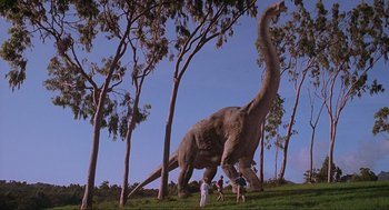 Movie still from “Jurassic Park” (1993), directed by Steven Spielberg – A large dinosaur in the middle of a field with trees; Extreme Wide shot, Low angle