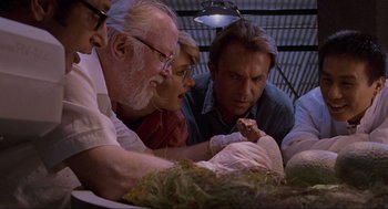 Movie still from “Jurassic Park” (1993), directed by Steven Spielberg – A group of people looking at a baby in a cage; Close Up shot, Low angle