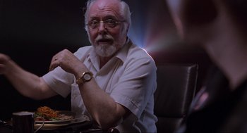 Movie still from “Jurassic Park” (1993), directed by Steven Spielberg – An older man sitting in front of a plate of food; Close Up shot, Over the shoulder angle