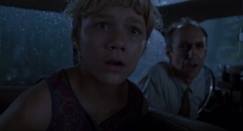 Movie still from “Jurassic Park” (1993), directed by Steven Spielberg – A young boy sitting next to an older man in a car; Close Up shot, Over the shoulder angle