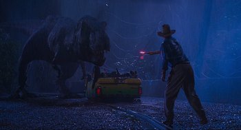 Movie still from “Jurassic Park” (1993), directed by Steven Spielberg – A man holding a red light while standing next to a dinosaur; Wide shot, Over the shoulder angle