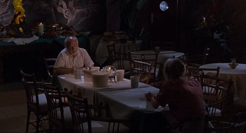 Movie still from “Jurassic Park” (1993), directed by Steven Spielberg – A man and woman sitting at a dinner table; Wide shot, High angle