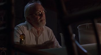Movie still from “Jurassic Park” (1993), directed by Steven Spielberg – An older man sitting at a table in a dark room; Close Up shot, Low angle