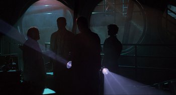 Movie still from “Jurassic Park” (1993), directed by Steven Spielberg – Three people are standing in a dark room with lights; Wide shot, Low angle