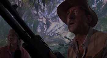 Movie still from “Jurassic Park” (1993), directed by Steven Spielberg – A man in a hat holding a rifle in a forest; Close Up shot, Low angle