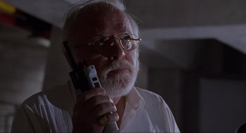 Movie still from “Jurassic Park” (1993), directed by Steven Spielberg – An older man with a beard and glasses holding a cell phone; Close Up shot, Low angle