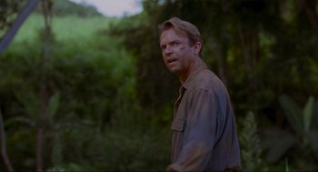 Movie still from “Jurassic Park” (1993), directed by Steven Spielberg – A man in a brown shirt is standing in the woods; Close Up shot, Over the shoulder angle
