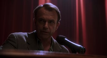 Movie still from “Jurassic Park III” (2001), directed by Joe Johnston – A man is speaking into a microphone in front of a red curtain; Close Up shot, Low angle