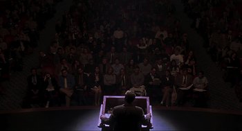 Movie still from “Jurassic Park III” (2001), directed by Joe Johnston – A man sitting in front of an audience in front of a projector; Extreme Wide shot, High angle