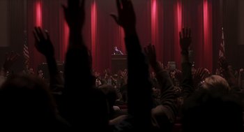 Movie still from “Jurassic Park III” (2001), directed by Joe Johnston – A crowd of people sitting in front of microphones in a room; Extreme Wide shot, High angle