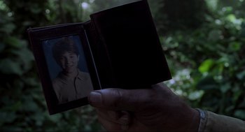 Movie still from “Jurassic Park III” (2001), directed by Joe Johnston – A person holding a photo of a man in front of a forest; Extreme Close Up shot, Over the shoulder angle