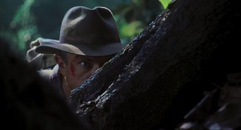 Movie still from “Jurassic Park III” (2001), directed by Joe Johnston – A man in a hat is peeking out from behind a tree; Close Up shot, Over the shoulder angle