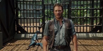 Movie still from “Jurassic World” (2015), directed by Colin Trevorrow – A man standing in front of a fence with a child sitting on the ground; Medium shot, Over the shoulder angle