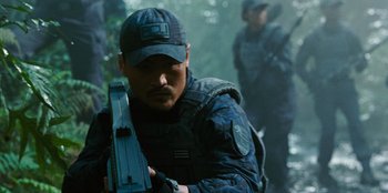 Movie still from “Jurassic World” (2015), directed by Colin Trevorrow – A man holding a gun while standing next to a forest; Medium shot, Over the shoulder angle