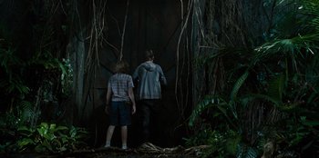Movie still from “Jurassic World” (2015), directed by Colin Trevorrow – Two people standing in the woods near a door; Wide shot, Low angle