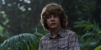 Movie still from “Jurassic World” (2015), directed by Colin Trevorrow – A young boy in a plaid shirt is standing in the woods; Close Up shot, Low angle