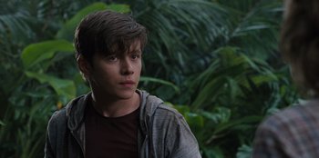 Movie still from “Jurassic World” (2015), directed by Colin Trevorrow – A young man standing in front of a lush green forest; Close Up shot, Over the shoulder angle