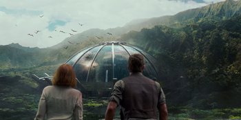 Movie still from “Jurassic World” (2015), directed by Colin Trevorrow – A man and a woman standing in front of a building with birds flying around it; Wide shot, Low angle