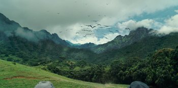 Movie still from “Jurassic World” (2015), directed by Colin Trevorrow – A flock of birds flying over a lush green hillside; Extreme Wide shot, High angle