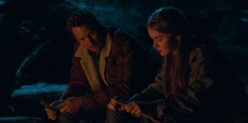 Movie still from “Jurassic World Dominion” (2022), directed by Colin Trevorrow – A man sitting next to a woman holding a stick; Medium shot, Over the shoulder angle