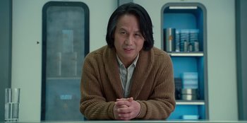 Movie still from “Jurassic World Dominion” (2022), directed by Colin Trevorrow – A man sitting at a table with his hands crossed; Medium shot, Low angle