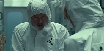 Movie still from “Jurassic World Dominion” (2022), directed by Colin Trevorrow – A man in a white lab coat is looking into a mirror; Medium shot, Over the shoulder angle